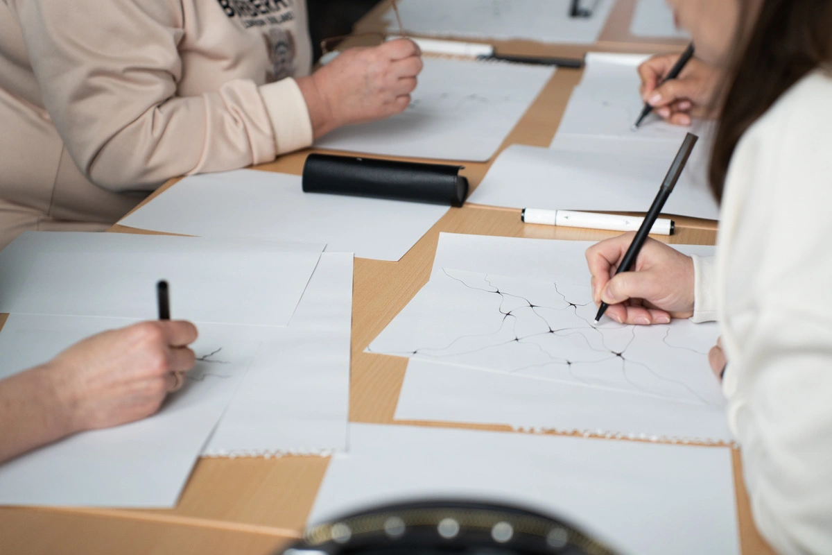 Participants dessinant des motifs abstraits sur des feuilles, représentant un atelier de dessin-thérapie pour explorer et exprimer les émotions.